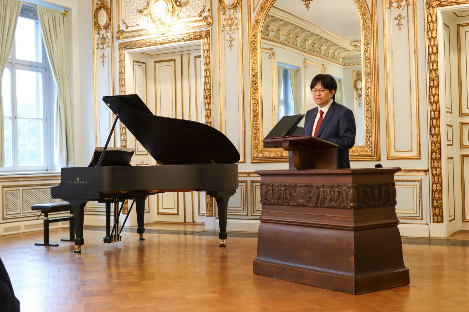 Ming Cheng speaking at the lectern at the German-Qatar Forum Saxony in the Old Senate Hall of Leipzig University